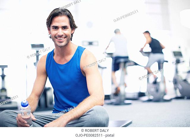 Portrait of smiling man sitting on exercise mat in gymnasium