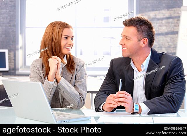 Happy businesspeople smiling at each other, sitting at desk, working together