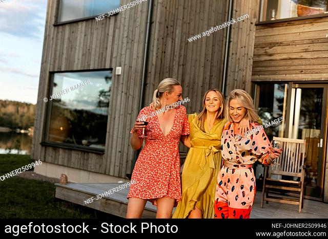 Smiling female friends holding wine glasses in backyard