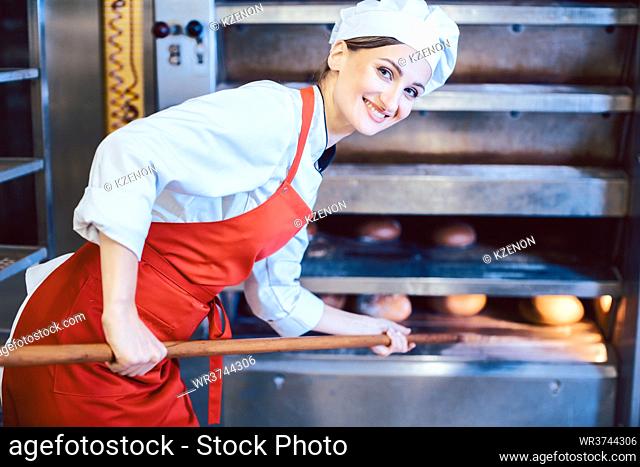 Baker woman getting fresh bread out of the oven, looking into camera