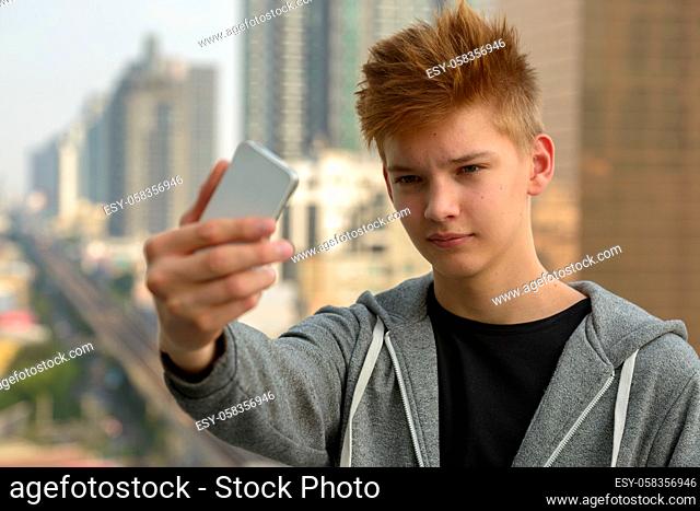 Portrait of young handsome teenage boy against view of the city outdoors