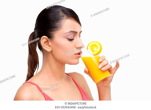 Close-up of young woman drinking orange juice over white background