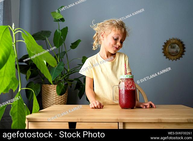 Girl making puckering face looking at smoothie in living room