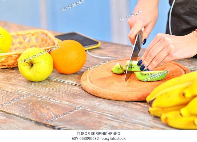 Hands of young girl in sportswear cutting kiwi on chopping board and listens to music