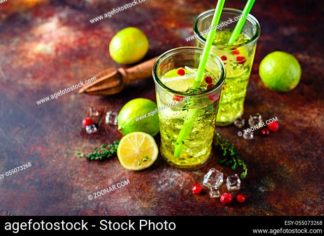 Two glasses with Lime Lemonade with thyme, cranberry and ice on light background. Refreshing summer homemade Alcoholic or non-alcoholic cocktails or Detox...