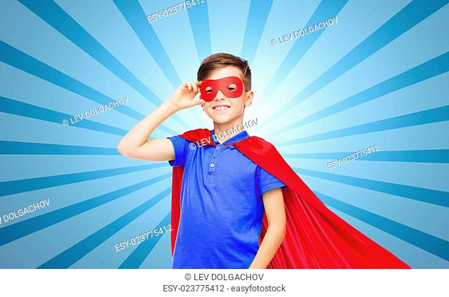 carnival, childhood, power, gesture and people concept - happy boy in red super hero cape and mask over blue burst rays background