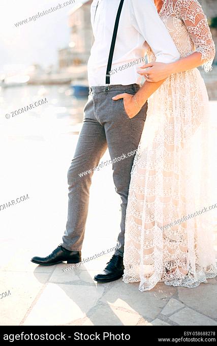 Bride hugs groom from behind while standing on the pier against the background of the port. Bottom view. High quality photo