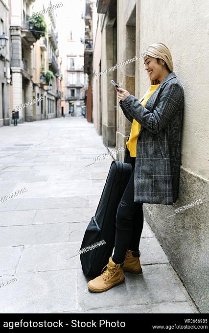 Young woman with violin case using smartphone in city