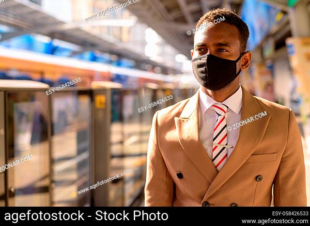 Portrait of young African businessman with mask for protection from corona virus outbreak social distancing at the skytrain station