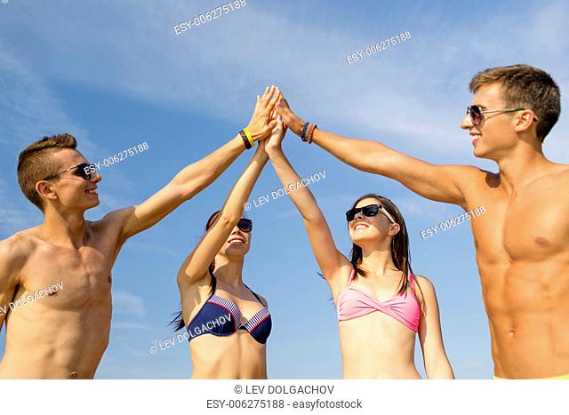friendship, sea, holidays, gesture and people concept - group of smiling friends wearing swimwear and sunglasses making high five on beach