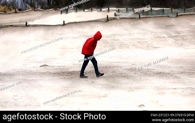 21 December 2023, Mecklenburg-Western Pomerania, Warnemünde: A man walks along the Baltic Sea beach in the storm, the wind-blown sand glowing brightly