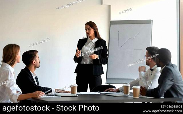 Confident Caucasian millennial businesswoman stand talking leading business meeting with colleagues, young female coach or presenter speak interact with...
