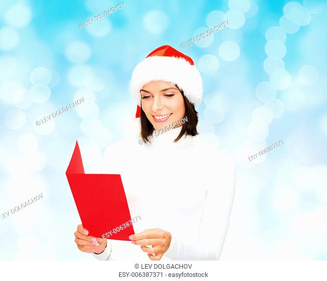 christmas, holidays, celebration, greeting and people concept - smiling woman in santa helper hat with greeting card over blue lights background