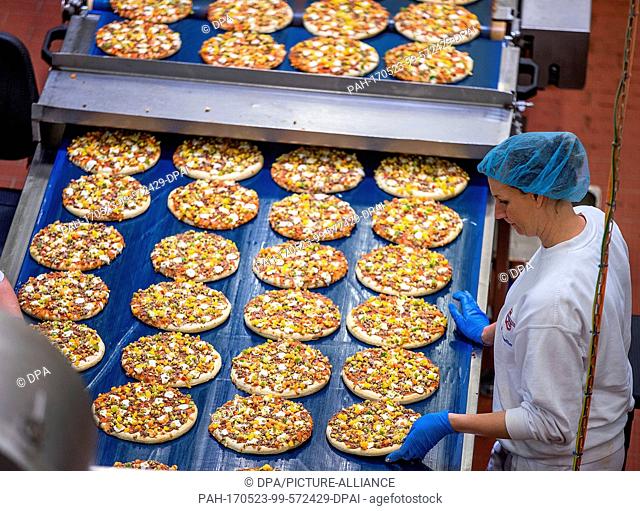 Employees cover pizza crusts with vegetable pieces in the pizza factory of the Dr. Oetker company in Wittenburg, Germany, 23 May 2017