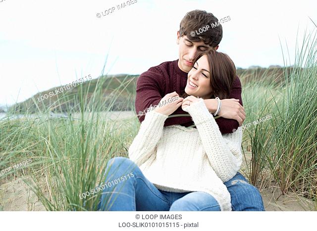 A young couple cuddling in the dunes on the beach at Porthmadog