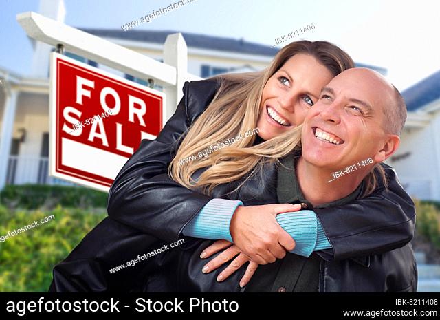 Happy couple hugging in front of for sale real estate sign and house