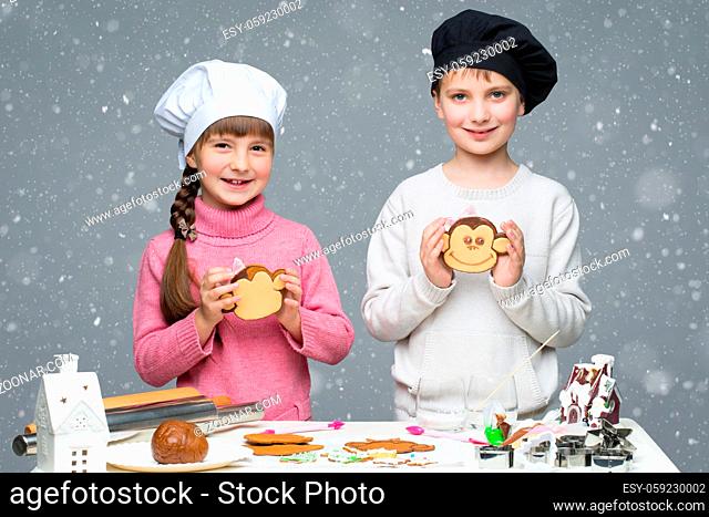 Beautiful boy and girl in chef hats holding monkey shape christmas cookie. Children standing iover snowy background