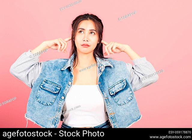 Asian portrait beautiful cute young woman wear denim plugging ears with fingers doesn't want to listen, studio shot isolated on pink background