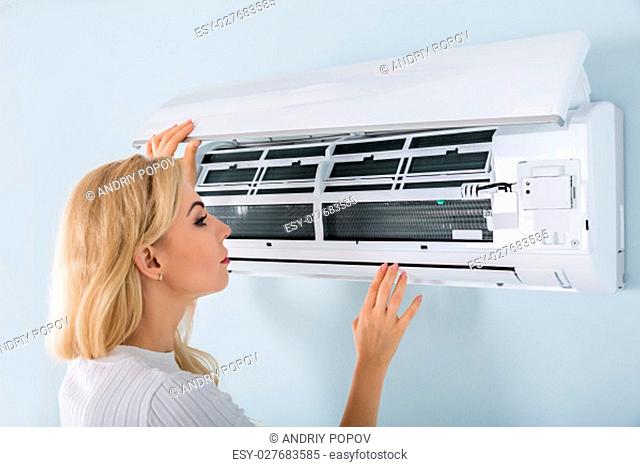 Young Woman Checking Air Conditioner Mounted On Wall At Home