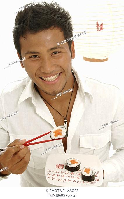 Asian man is eating sushi with chopsticks