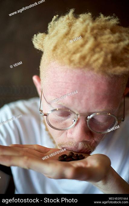 Albino man in a cafeteria smelling coffee beans in hand