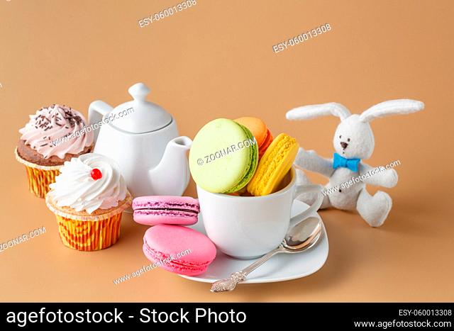 Colorful French macaroons and cup of tea on beige background. Kid party decoration