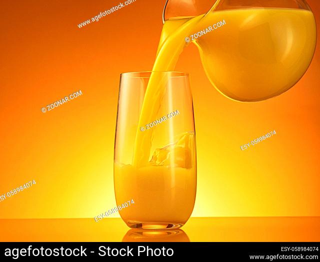 Orange juice pouring from jug into glass over color background with copy space