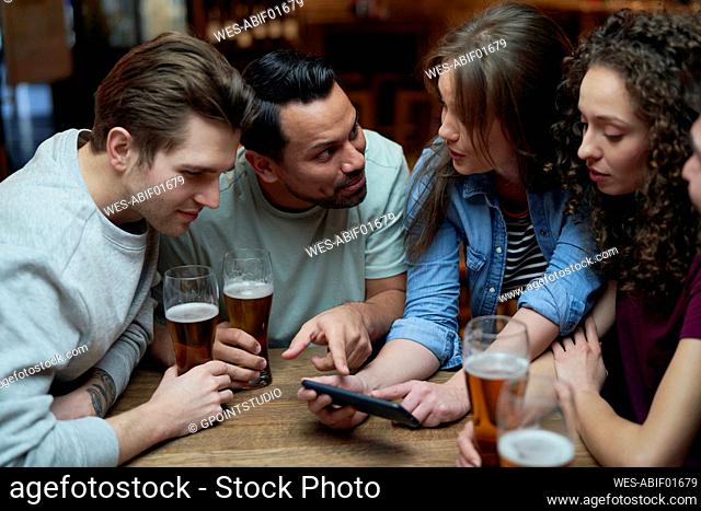 Group of friends having beer and sharing a smartphone in a pub