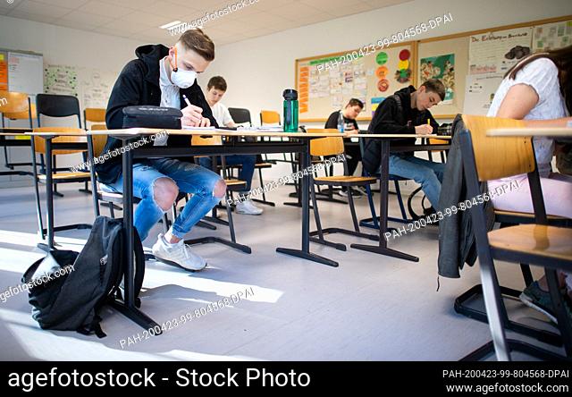 23 April 2020, North Rhine-Westphalia, Ìbach-Palenberg: Pupils, one of them wearing a protective mask, work on computer science tasks in the basic computer...