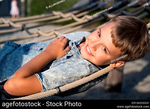Blond boy smiling and looking at the camera while lying on a rope playground in a public park