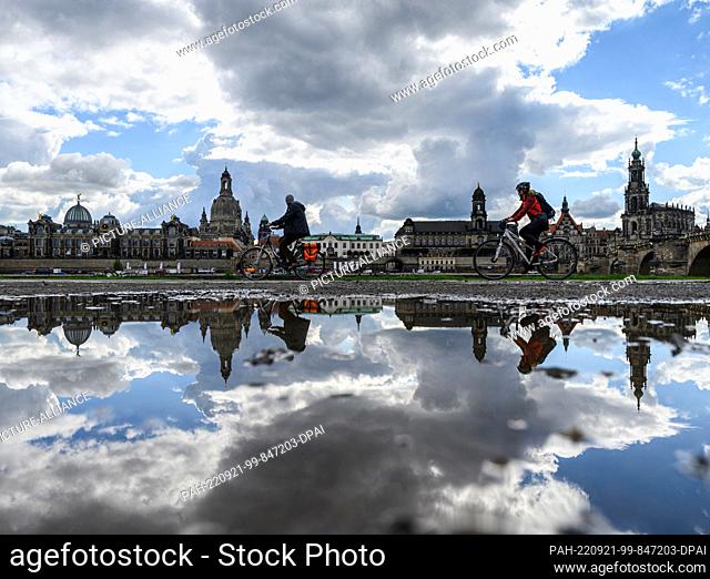 21 September 2022, Saxony, Dresden: Cyclists are on the Elbe cycle path opposite the historic old town backdrop with the dome of the Kunstakedmie with the angel...