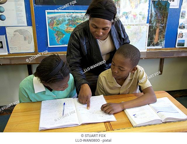 Teacher assists two pupils with their classwork, KwaZulu Natal Province, South Africa