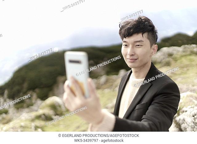 Korean man looking at smartphone during hiking trip in Austrian mountains, Europe, Austria, Salzburg, Mount Untersberg