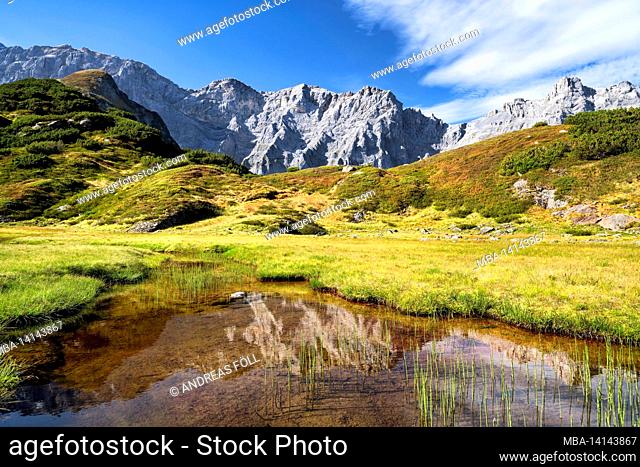 idyllic mountain landscape with a small pond in front of steep rocky mountains above the erstfeldertal near the kröntenhütte on a sunny day in autumn
