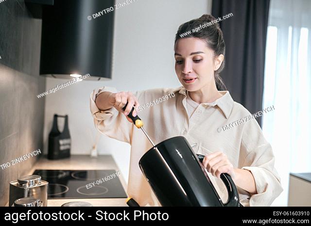 Broken kettle. A young dark-haired woman holding a broken kettle in her hands