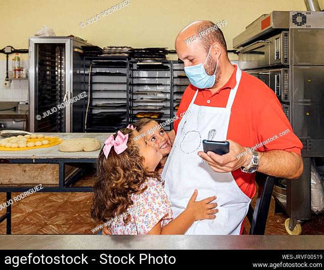 Daughters hugging father with protective face mask at bakery