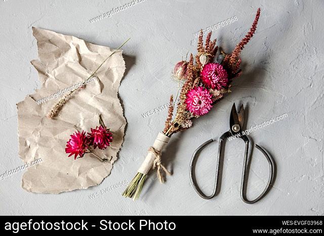 Studio shot of scissors, piece of paper and small bouquet of dried flowers