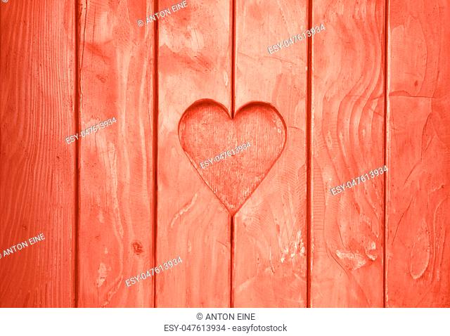 Close up one heart shape, symbol of love and romance, wood carved cut in wooden planks texture background, coral pink painted window shutter