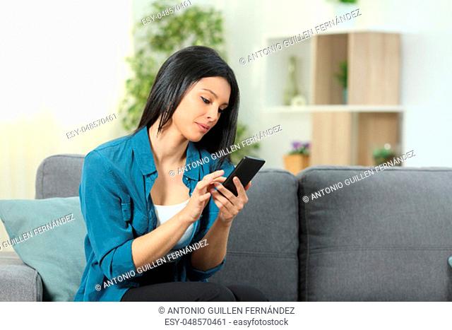 Serious woman using a smart phone sitting on a couch in the living room at home