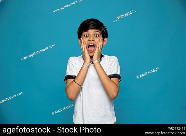 Portrait of shocked boy standing against blue background