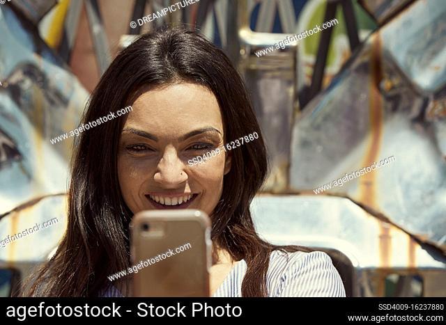Young woman in front of chrome sculpture using mobile phone to take selfie