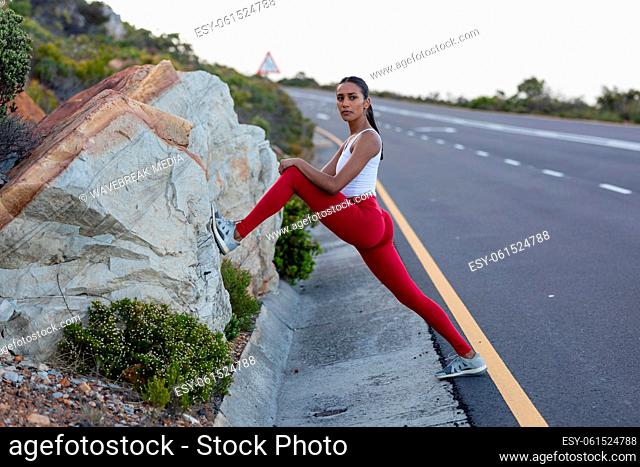 Fit african american woman in sportswear stretching on a coastal road
