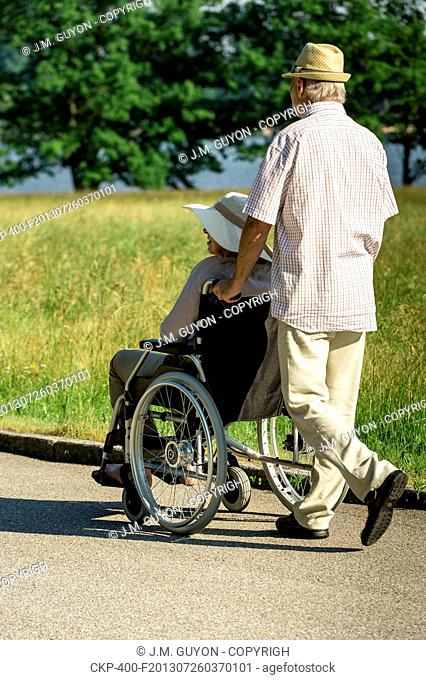 Senior husband pushing wife's wheelchair in park