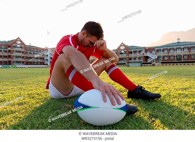 Male rugby player sitting with rugby ball in the ground