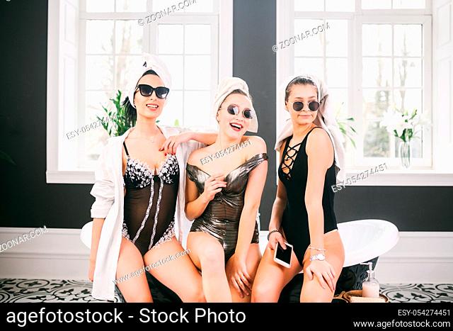 Theme female friendship. Party girlfriends, relaxation and spa procedures, hen party. Three Caucasian beautiful women sitting inside on bathroom in sunglasses