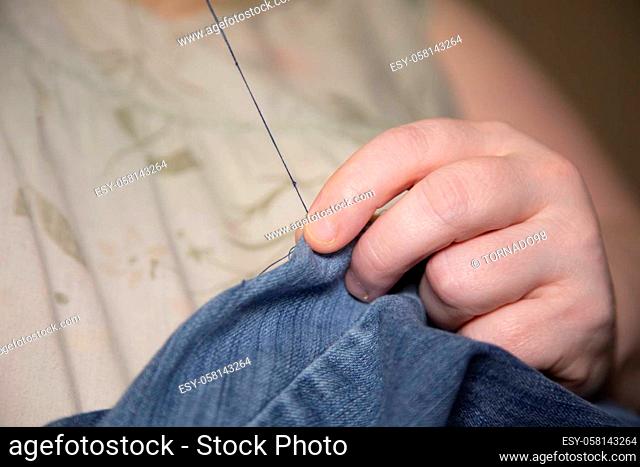 Woman sewing denim blue jeans with blue thread