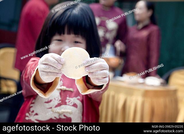 Little girl showing dumpling wrapper in traditional clothing