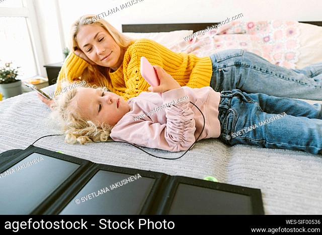 Mother looking at daughter watching mobile phone in bedroom