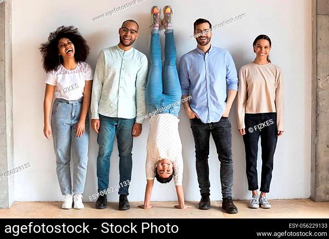 Portrait of overjoyed young people near white wall with happy indian woman standing on upside down on hands. Group of smiling multiracial best friends having...