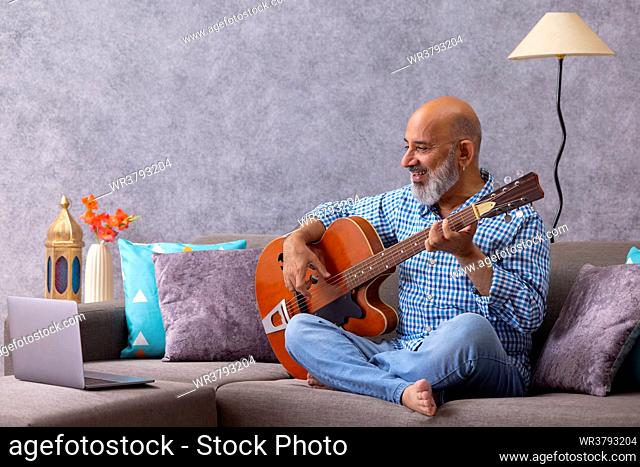 Senior man having online guitar lesson through laptop